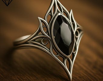 May include: A silver-toned ring featuring an intricate, openwork metal design with a pointed, marquise-shaped black gemstone set in the center. The metalwork displays a series of curved, leaf-like filigree patterns that extend outward from the stone.