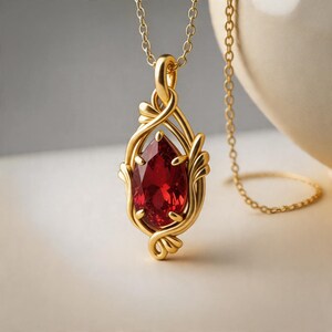May include: A gold pendant necklace featuring a pear-shaped, deep red gemstone set within an intricate, swirling gold frame. The pendant hangs from a delicate gold chain, showcasing a polished metallic finish and a faceted, vibrant red stone.