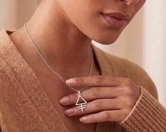 May include: A silver-toned necklace featuring a pendant shaped like an equilateral triangle with two horizontal lines crossing the bottom point. The pendant hangs from a delicate, thin silver-toned chain resting against a textured tan-colored fabric.