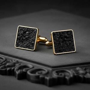 May include: A pair of square cufflinks featuring a textured black surface set within a polished gold-tone metal frame. Each cufflink has a gold-tone post and toggle mechanism extending from the back of the square face for secure attachment.