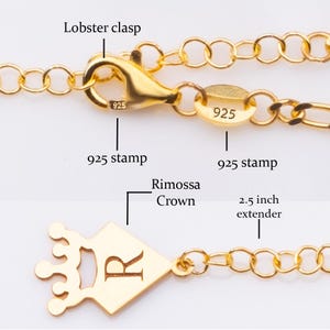 K&ouml;nnte beinhalten: Nahaufnahme einer goldfarbenen Halskette mit Karabinerverschluss und einem 6,35 cm Verl&auml;ngerungsst&uuml;ck. Die Halskette hat einen kronenf&ouml;rmigen Anh&auml;nger mit dem Buchstaben "R" und einem "925" Stempel. Die Kette besteht aus kleinen, verbundenen Gliedern.