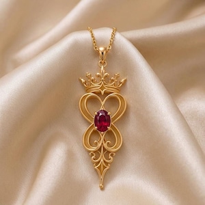 May include: A gold pendant necklace featuring a central oval-shaped deep red gemstone. The pendant design includes an ornate crown motif at the top, connected to a delicate gold chain, with intricate swirling metalwork surrounding the stone.