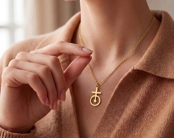 May include: A gold-toned necklace featuring a delicate chain and a pendant shaped like a circle with a cross extending from the top and a small dot centered within the circular base. The metal has a smooth, polished finish throughout the piece.