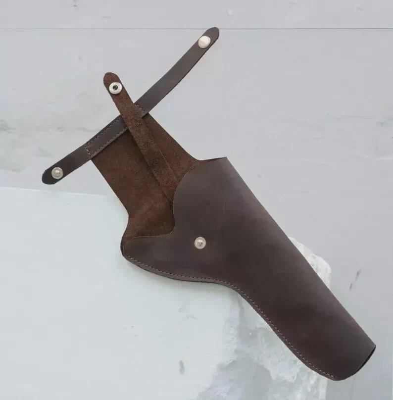 May include: A brown leather quiver with a suede interior. The quiver has a long, tapered shape with a curved side and a strap that fastens with silver-colored rivets. The design suggests it is for archery.