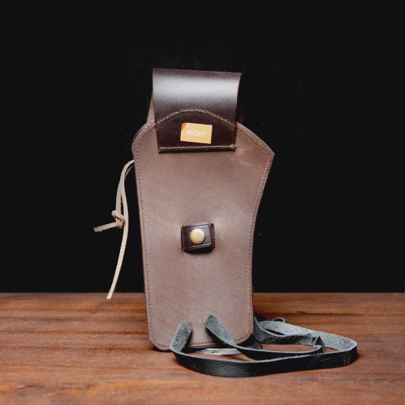 May include: A brown leather holster with a dark brown flap and strap. The word "RIGHT" is visible on a small tag. The holster has a button closure and a leather strap for carrying. The holster is designed to hold a firearm.