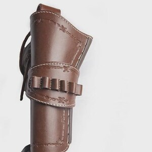 May include: A brown leather holster with decorative stitching and a cartridge belt. The holster is designed to hold a firearm and features a loop for a belt. The leather is a rich, dark brown color with white stitching.