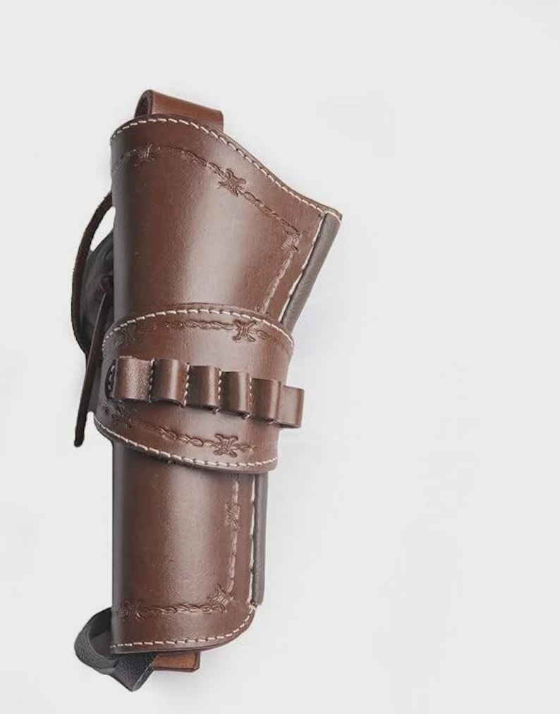 May include: A brown leather holster with decorative stitching and a cartridge belt. The holster is designed to hold a firearm and features a loop for a belt. The leather is a rich, dark brown color with white stitching.