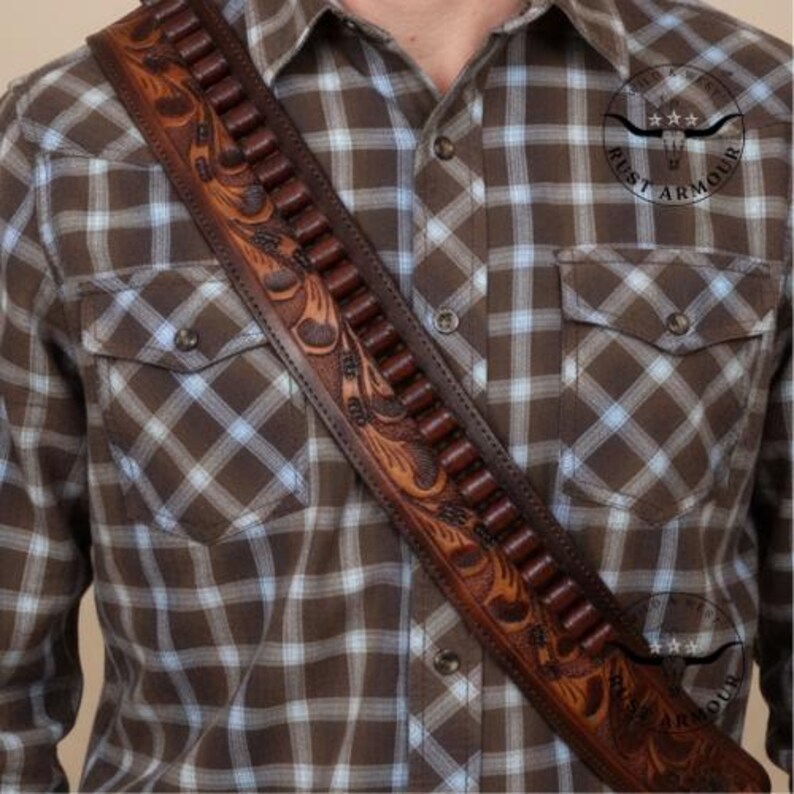 May include: A brown leather cartridge belt with detailed floral carving. The belt, worn diagonally, has many bullet loops. The background is a brown and blue checked shirt.