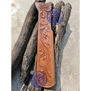 Puede incluir: Una funda de cuero marrón claro hecha a mano con intrincados tallados florales y de volutas. La funda está diseñada para guardar un objeto largo y estrecho, posiblemente un cuchillo o una herramienta. El cuero tiene un acabado natural y está cosido en los bordes.