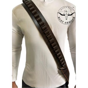 May include: A dark brown leather bandolier with multiple cartridge loops. The bandolier is worn over the shoulder and across the chest. The image also features a white long-sleeve shirt and a logo that says "Wild & West Rust Armour".