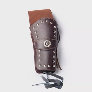 May include: A brown leather holster with silver studs and a star-shaped emblem. The holster has a belt loop and a strap. The design is reminiscent of the Wild West. The holster is made of leather.