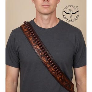 May include: A brown leather cartridge belt with a floral tooled design, worn diagonally across the chest. The belt has multiple cartridge loops and is made of dark brown leather. The image includes the "Rust Armour" logo.