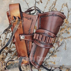 May include: A set of brown leather gun holsters with decorative stitching and a cartridge belt. The holsters are designed to be worn on the hip and are secured with straps and a buckle. The leather has a rich, aged appearance.