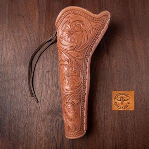Peut inclure: Un étui en cuir marron avec des motifs floraux. L'étui présente un motif floral décoratif et une lanière en cuir. Le logo Wild & West Armour est visible en bas à droite. L'étui est présenté sur une surface en bois.