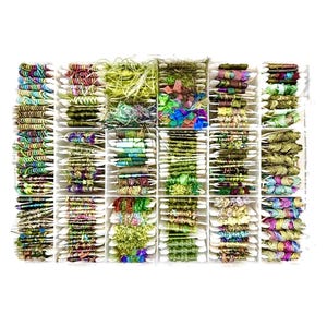 May include: A rectangular white plastic organizer tray filled with numerous small white cardboard bobbins, each wrapped with various colorful decorative yarns, ribbons, and textured fibers in shades of green, pink, blue, and metallic gold.
