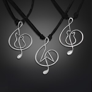 K&ouml;nnte beinhalten: Drei silberne Halsketten mit schwarzen Schn&uuml;ren. Jede Halskette hat einen  Treble-Clef-Anh&auml;nger mit einem anderen Design innerhalb des Schl&uuml;ssels. Der erste Anh&auml;nger hat eine Gitarre innerhalb des Schl&uuml;ssels, der zweite Anh&auml;nger hat ein Peace-Zeichen innerhalb des Schl&uuml;ssels und der dritte Anh&auml;nger hat eine Katze innerhalb des Schl&uuml;ssels.