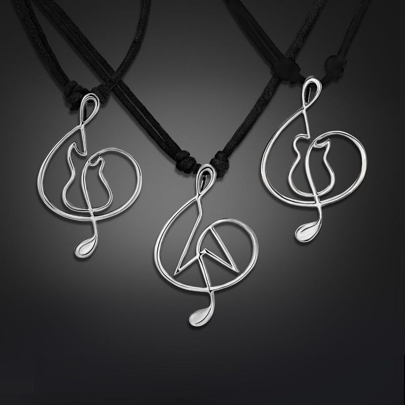 K&ouml;nnte beinhalten: Drei silberne Halsketten mit schwarzen Schn&uuml;ren. Jede Halskette hat einen  Treble-Clef-Anh&auml;nger mit einem anderen Design innerhalb des Schl&uuml;ssels. Der erste Anh&auml;nger hat eine Gitarre innerhalb des Schl&uuml;ssels, der zweite Anh&auml;nger hat ein Peace-Zeichen innerhalb des Schl&uuml;ssels und der dritte Anh&auml;nger hat eine Katze innerhalb des Schl&uuml;ssels.