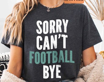 May include: A dark gray t-shirt with the text "Sorry Can't Football Bye" in white and green lettering.
