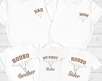 May include: A set of five white t-shirts with brown text and a bull skull graphic. The shirts say "Dad", "Mom", "Rodeo Brother", "My First Rodeo", and "Rodeo Sister".