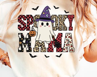 May include: A cream-colored t-shirt with the words "Spooky Mama" in a mix of fonts and patterns. The design includes a ghost wearing a witch hat, holding a pumpkin, and a broom. Black bats are scattered around the text.