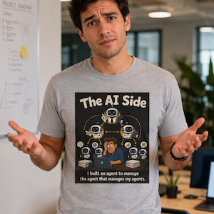 Op de afbeelding: Lichtgrijs t-shirt met een afbeelding van "The AI Side", met cartoonrobots en een persoon met een laptop. De tekst "I built an agent to manage the agent that manages my agents" is ook zichtbaar.