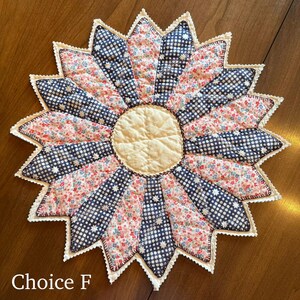 May include: A handmade, starburst-shaped quilted item with a cream-colored center and alternating segments of floral and navy blue star-patterned fabric. The edges are finished with a white, scalloped trim. The text "Choice F" is at the bottom.
