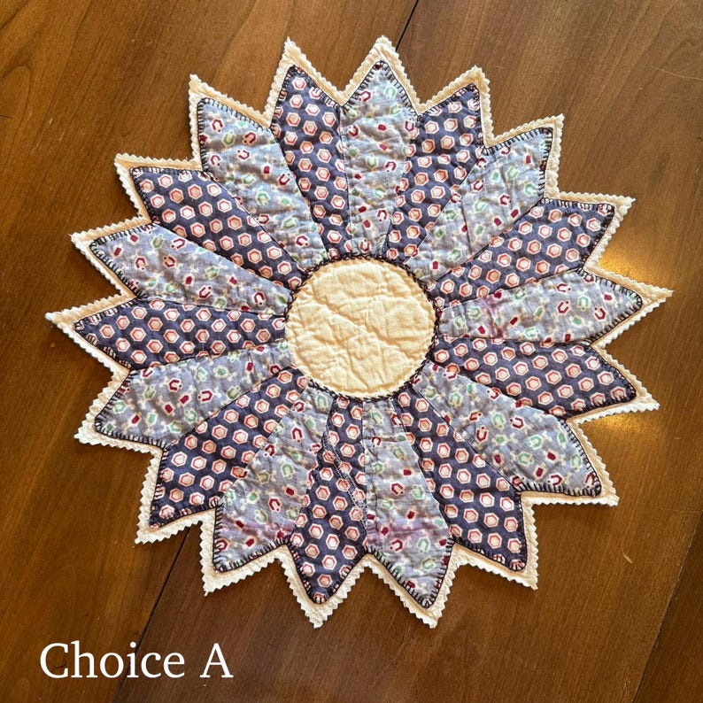 May include: A handmade, quilted sunflower-shaped trivet. The trivet features a cream-colored center and petals in shades of blue and patterned fabric. The edges are finished with a white, scalloped trim. The text "Choice A" is at the bottom.