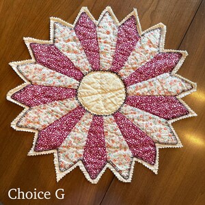 May include: A handmade, quilted sunflower-shaped placemat. The design features alternating burgundy floral and cream-colored floral fabric segments, with a cream-colored center and scalloped edges. The text "Choice G" is in the lower left corner.