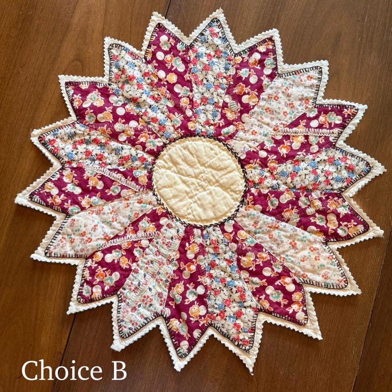 May include: A handmade, starburst-shaped quilted placemat. The center is a cream-colored circle, surrounded by burgundy and floral print segments. The edges are finished with white lace and the text "Choice B".
