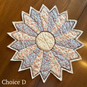 May include: A handmade, starburst-shaped quilted trivet with a cream-colored center and alternating sections of floral and patterned fabric in shades of blue, peach, and cream. The edges are scalloped with a white trim and the text "Choice D" is visible.
