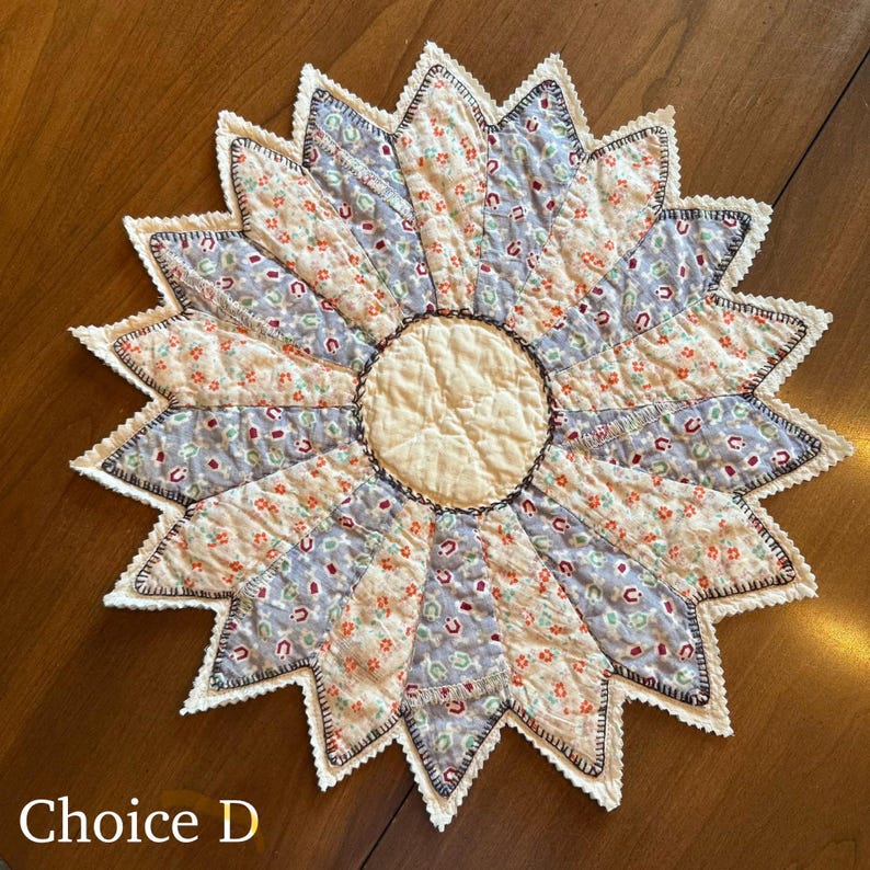 May include: A handmade, starburst-shaped quilted trivet with a cream-colored center and alternating sections of floral and patterned fabric in shades of blue, peach, and cream. The edges are scalloped with a white trim and the text "Choice D" is visible.