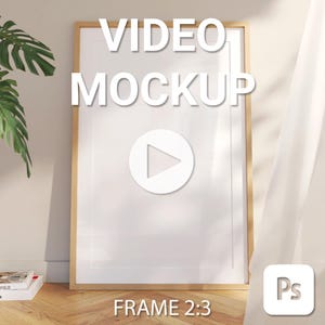May include: A wooden frame mockup with a white background and a play button icon. The text "VIDEO MOCKUP" is at the top of the frame and "FRAME 2:3" is at the bottom. The frame is on a wooden floor with a plant and a white curtain in the background.