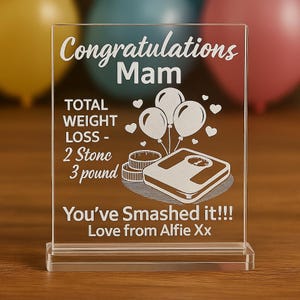 May include: Clear acrylic plaque with the words "Congratulations Mam" and "You've Smashed it!!!" etched in white. The plaque includes an illustration of a scale, balloons, and hearts. The text also mentions a total weight loss of 14 kg.