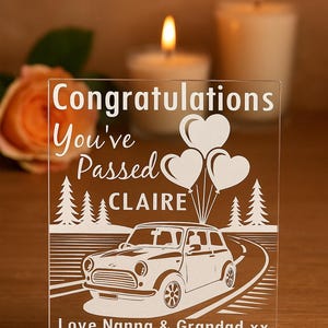 May include: Clear acrylic graduation gift with white etched design. Text reads "Congratulations You've Passed CLAIRE" with heart balloons, trees, and a car. Bottom text says "Love Nanna & Grandad xx".