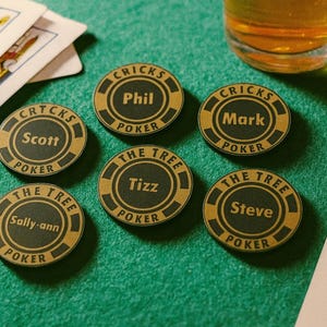 May include: A selection of personalised poker chips with names such as Phil, Mark, and Scott, are displayed on a green felt surface. The chips feature gold and black detailing and the text "CRICKS POKER" and "THE TREE POKER". Playing cards and a beer glass are also present.