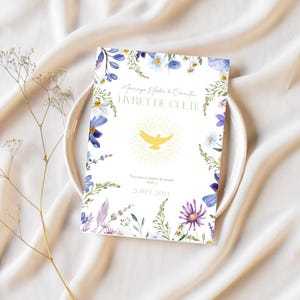 Peut inclure: Un livret blanc avec une bordure florale et le texte "Mariage Elodie & Camille LIVRET DE CULTE 21 SEPT 2021" en lettres dorées. Une colombe jaune avec une auréole est au centre du livret.