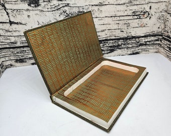 May include: An open book with a rectangular cutout, likely for storage. The interior features a gold and green patterned design. The book's cover is a dark green color, and the pages are white.