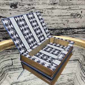 May include: A decorative book with a hollowed-out interior, featuring a geometric black, white, and light green pattern on the inside covers. The book's pages have a golden hue, and the edges are blue.