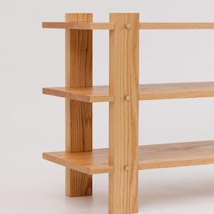 May include: A wooden shelf unit with three shelves and four legs. The shelves are made of light wood and the legs are made of a darker wood.