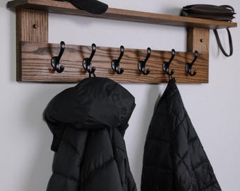 May include: A wooden coat rack with a shelf and six hooks. The rack is stained a dark brown and has a natural wood grain. Two black jackets are hanging on the hooks. A brown leather wallet is on the shelf.