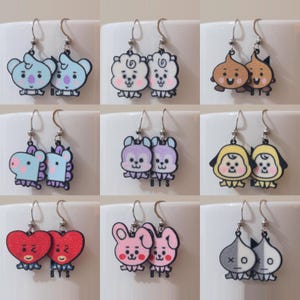 May include: Nine pairs of dangle earrings featuring various cartoon characters. Each pair has two earrings with the same design. The characters include a unicorn, a bunny, a sheep, a dog, and a bear. The earrings are made of metal and have a silver finish.