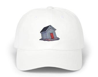 May include: White baseball cap featuring an embroidered design of a small, gray wooden house with a red door and a dark blue roof. The house is set on a rocky base. The cap has a curved brim and an adjustable strap.