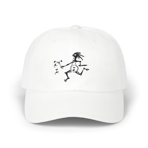 May include: A white baseball cap featuring a black graphic print of a stylized, spindly figure running while holding a pitchfork and a knife, accompanied by several small musical note symbols floating near the figure's outstretched hand.
