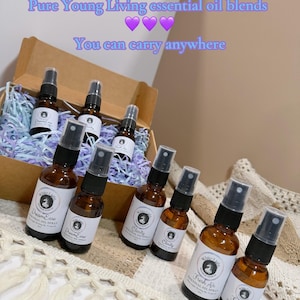Puede incluir: Botellas de spray de aceite esencial de vidrio ámbar, etiquetadas con nombres como "Dream Ease", "Clarity" y "Fresh Air". Las botellas están dispuestas en una caja de cartón y sobre una superficie estampada. Texto superpuesto: "Pure Young Living essential oil blends. You can carry anywhere."