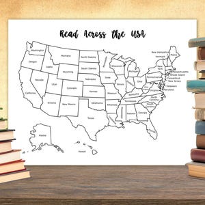 May include: A black and white map of the USA, labelled "Read Across the USA." The map shows state outlines. Stacks of books are on either side of the map. The map is on a white background, and the books are on a wooden surface.
