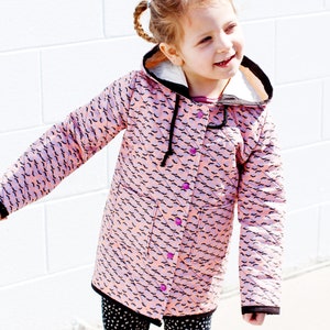 May include: A young girl wearing a pink hooded jacket with a black and white bat print. The jacket has a black zip and pink buttons. The girl is wearing black and white polka dot leggings.