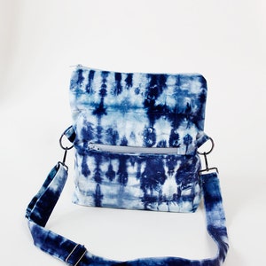 May include: A blue and white tie-dye fabric crossbody bag with a zippered pocket and adjustable strap.