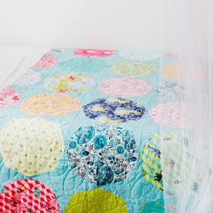 Op de afbeelding: Een turquoise blauwe quilt met een patchwork ontwerp met verschillende kleurrijke cirkels. De cirkels zijn gemaakt van verschillende stoffen met bloemen-, geometrische en stippenpatronen.