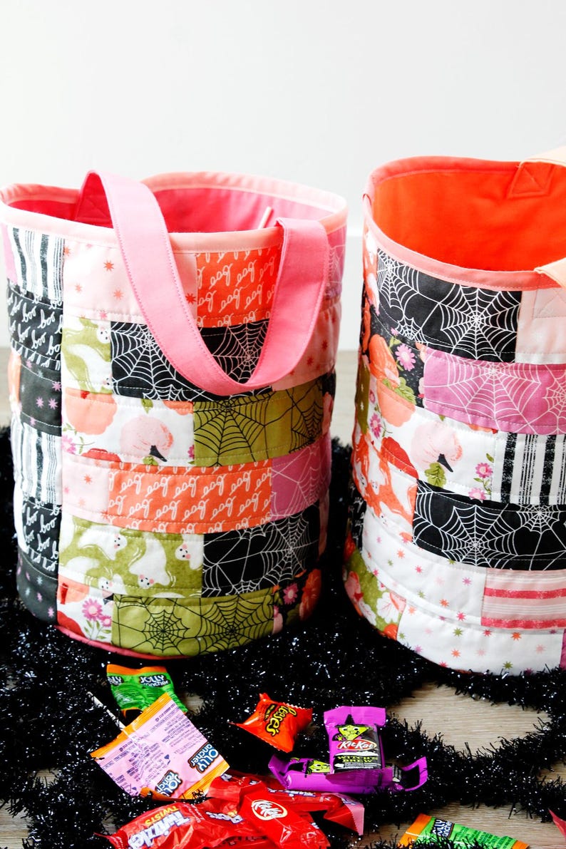 Puede incluir: Dos bolsas de tela de Halloween para pedir dulces de color rosa y naranja con dise&ntilde;os de patchwork que incluyen fantasmas, ara&ntilde;as y telara&ntilde;as. Las bolsas tienen asas rosas y est&aacute;n llenas de caramelos.