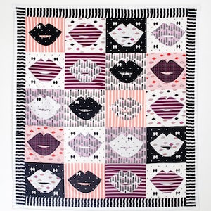 Puede incluir: Una colcha blanca con un borde negro y un patrón repetido de labios rosas, negros y blancos. Los labios están en varios patrones, incluyendo rayas, lunares e impresiones de lápiz labial.